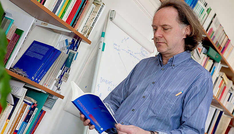 Soziologe Christoph Reinprecht mit offenen buch lesend vor einem Bücherregal