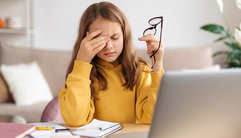 Foto von einer Teenagerin, die verzweifelt und gestresst am Schreibtisch sitzt.