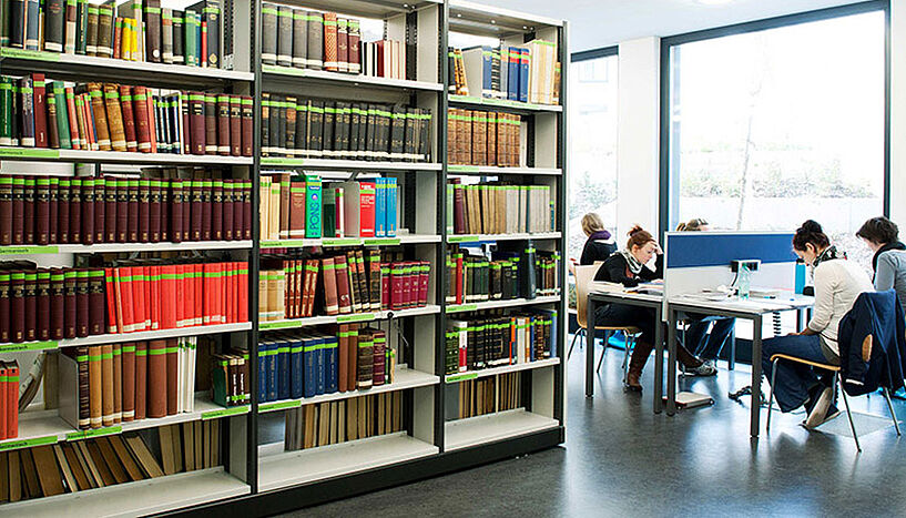Bücherregal und Studierende am Laptop in der Bibliothek