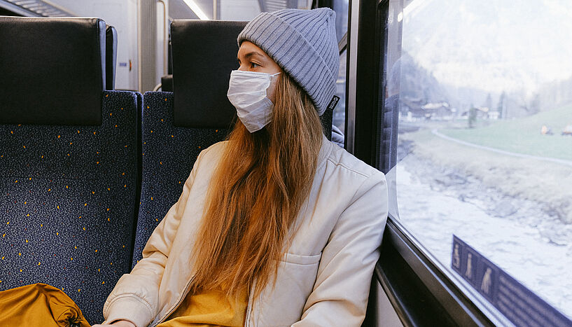 Frau mit Maske sitzt im Zug