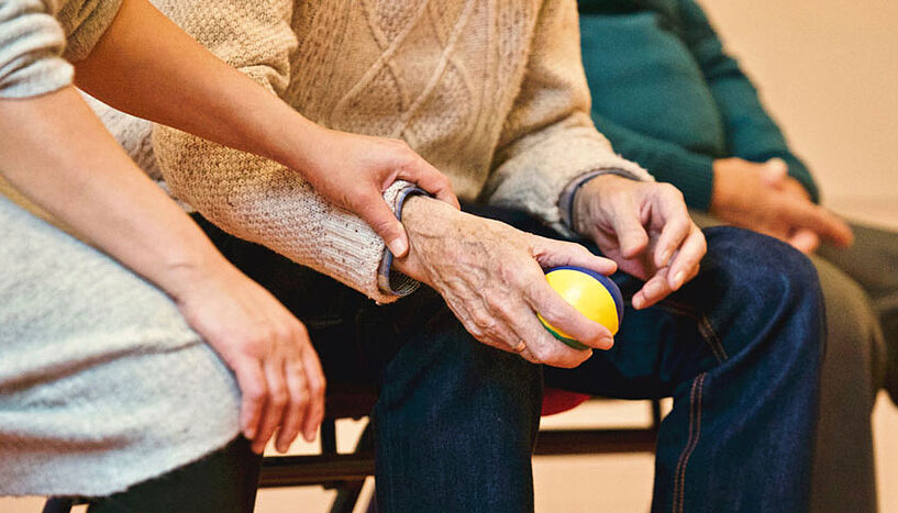Eine ältere Person hält einen Ball, daneben sitzt eine jüngere Person.